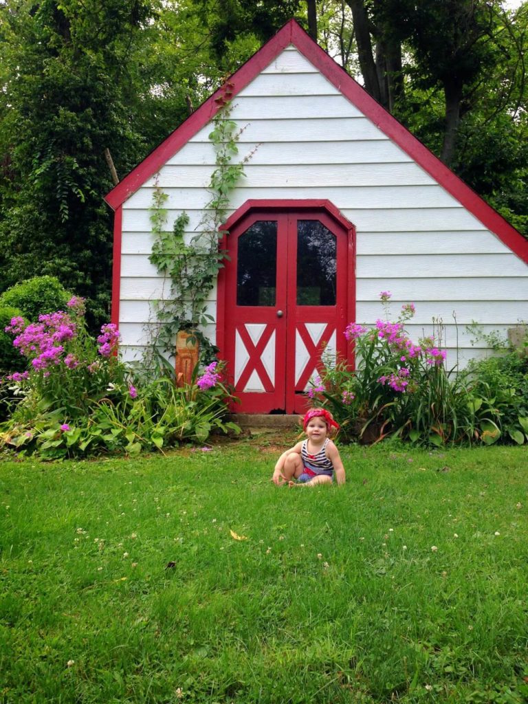 cute baby sitting by red and white shed
