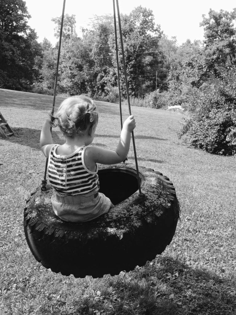 black and white picture of girl on tree swing