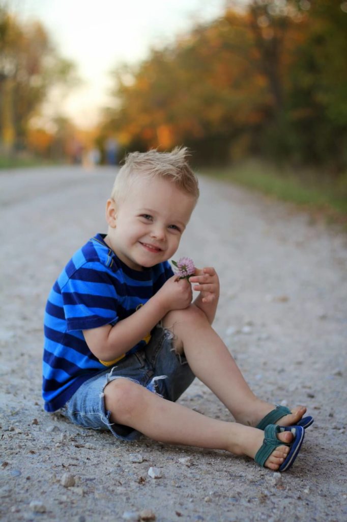 boy sitting and smiling holding little blue flower on walking trail