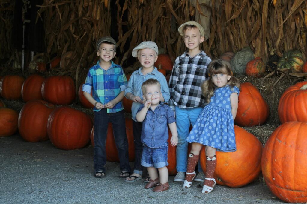 5 kids standing next to pumpkin display